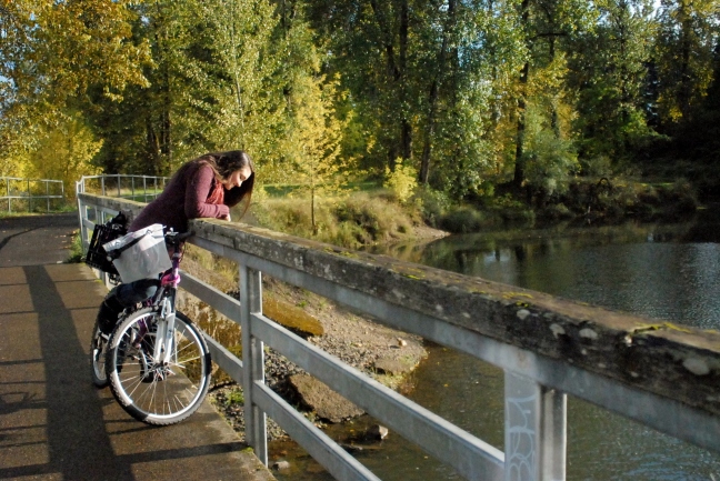 Girl on bike looking over bridge to duckpond